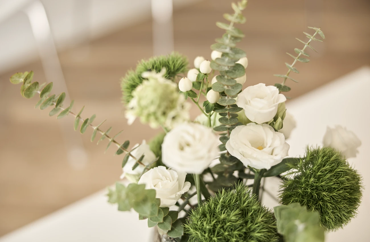 Blumenarrangement mit weißen Rosen und grünen Blättern in der Zahnarztpraxis Dr. Rothacher & Kollegen.