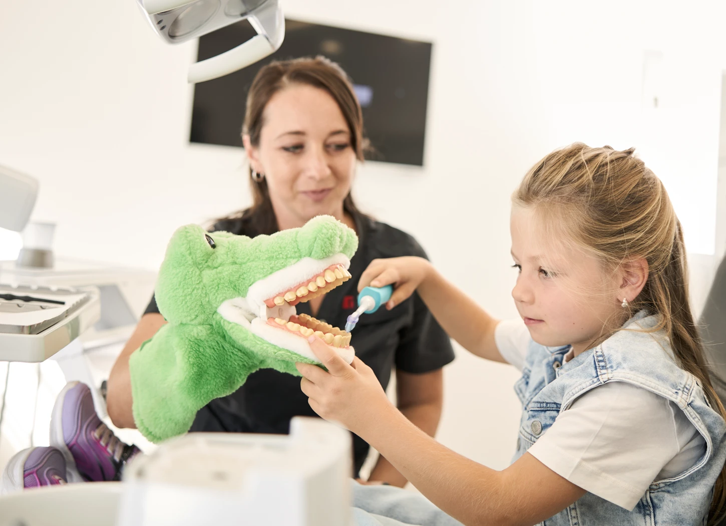 Kind übt Zähneputzen mit Krokodil-Handpuppe bei Zahnarzt Dr. Rothacher & Kollegen in Grünkraut.