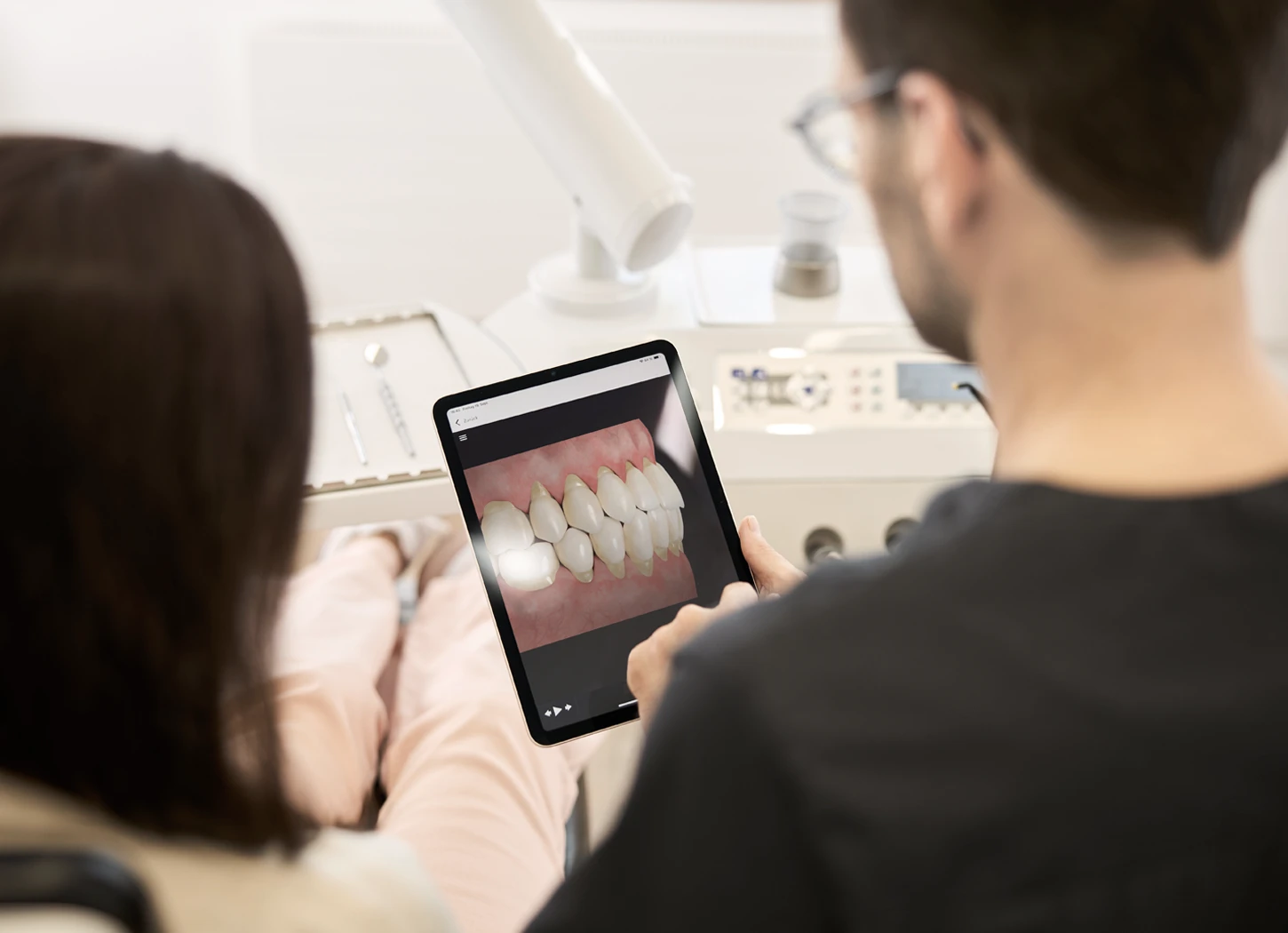 Zahnarzt zeigt Patientin Bild mit freiliegenden Zahnhälsen auf Tablet in moderner Praxis.