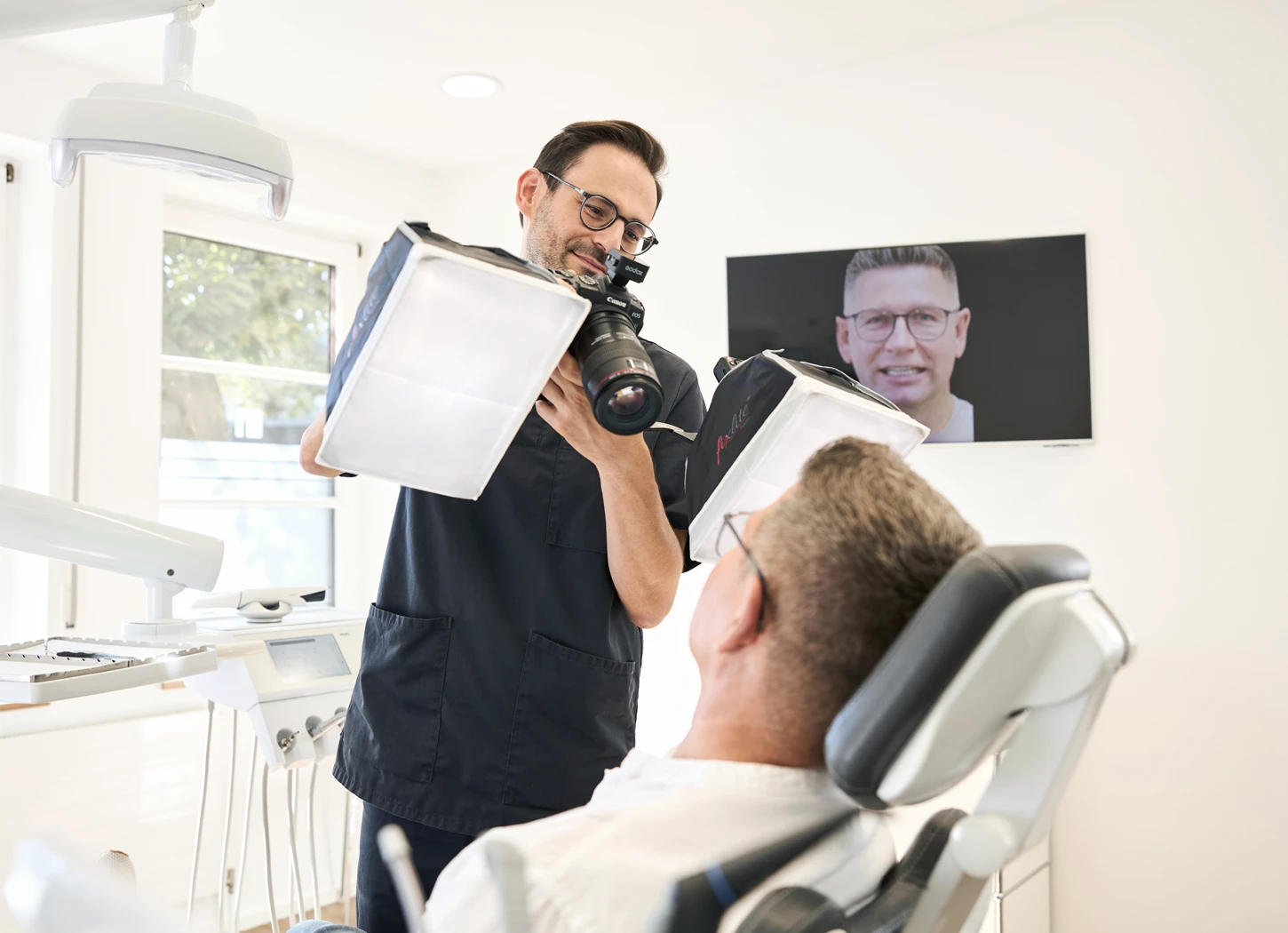 Zahnarzt Dr. Rothacher fotografiert sitzenden Patienten im hellen Behandlungszimmer.